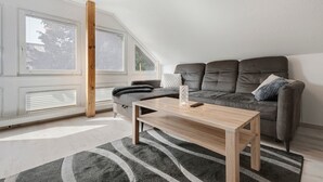 A modern loft bedroom with a sloped ceiling, a grey sofa, a wooden coffee table, and a grey rug.
