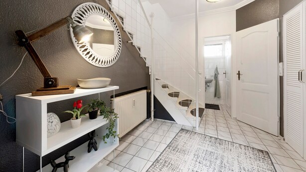 A modern interior with a white staircase, a round mirror, a white console table with decorative items, and a tiled floor.