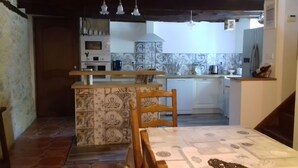 Cuina amb una illa central, taula de menjador i cadira de fusta.