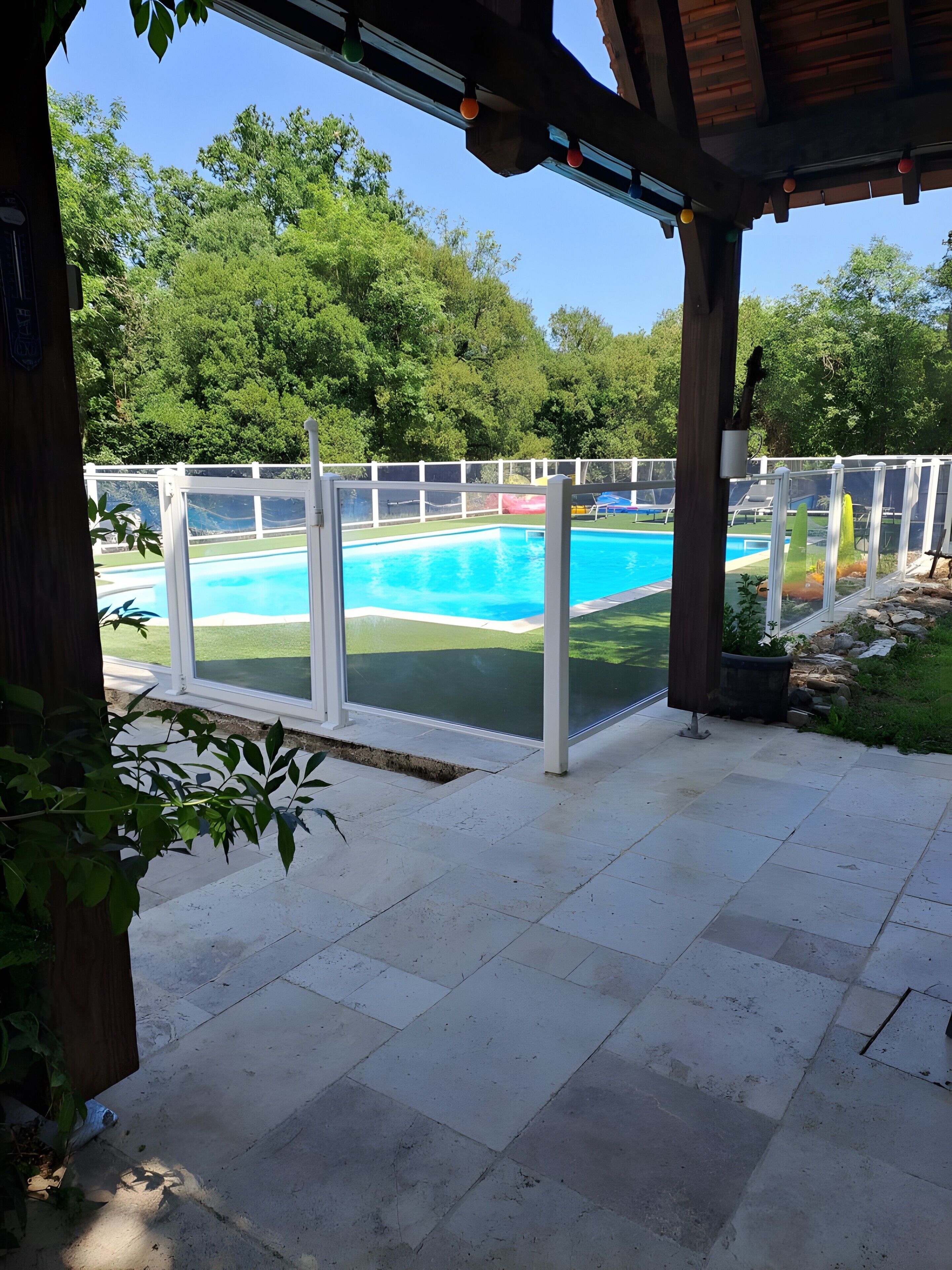Un porche cubierto con vistas a una piscina, valla blanca y follaje.
