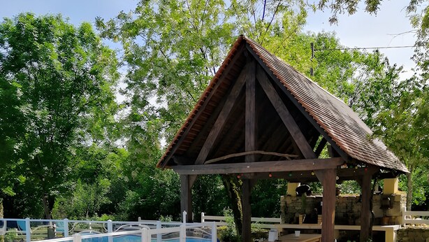 Zona d'estar exterior coberta amb piscina, mobles de fusta i una estructura de pergola.