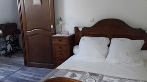Un dormitori amb un llit de fusta, una tauleta de nit, un armari i una porta.