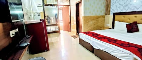 Una habitación de hotel con una cama, un escritorio, una televisión y un baño visible a través de una puerta abierta.