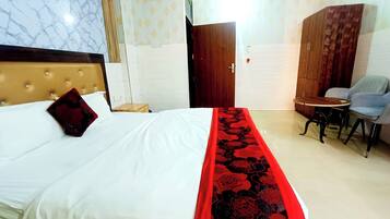 A hotel room with a bed, a wooden headboard, a red floral bedspread, a small round table with two chairs, and a wardrobe.