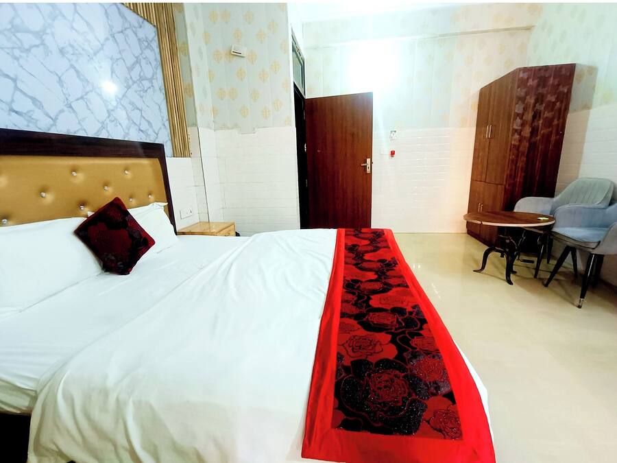 A hotel room with a bed, a wooden headboard, a red floral bedspread, a small round table with two chairs, and a wardrobe.
