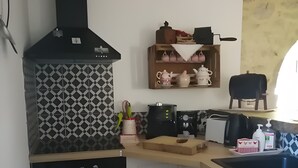 Una cocina con estufa y horno negros, y un salpicadero decorativo. Se ve una repisa con utensilios de cocina y un colgador para ollas.
