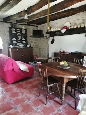 Un espace repas comprenant une table en bois, des chaises, un canapé rouge et un sol carrelé.