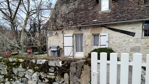Una casa de piedra con valla de piquetes blancos, una parrilla y un pequeño jardín.
