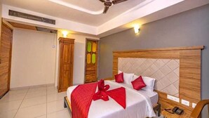Une chambre d’hôtel avec un lit, une tête de lit en bois, un ventilateur de plafond et une table de chevet avec un téléphone.