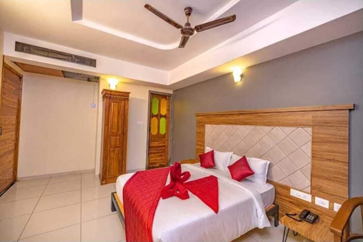 Habitación de hotel con cama, cabecera de madera, ventilador de techo y mesita de noche con teléfono.