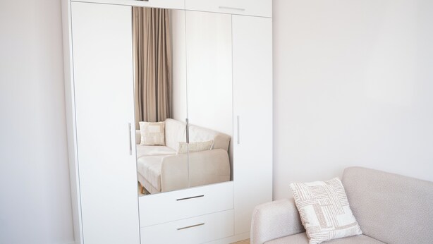 Un dormitorio moderno con un armario grande, una cama con edredón color beige y un sofá de tono claro con un cojín estampado.