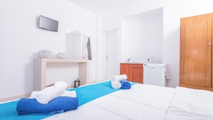 A hotel room with a bed, a wooden wardrobe, a small desk with a lamp, and a television on the wall. - 1-bed Apt at Bella Santorini, Near Perivolos Beach (Santorini)