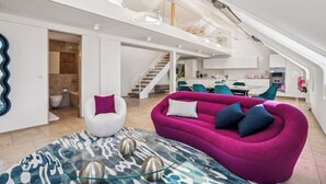 Amplia sala de estar con diseño moderno, que incluye un sofá rosa, una silla blanca y una alfombra estampada.