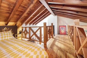 Une chambre aménagée dans les combles, avec un lit, une rambarde en bois et un escalier.