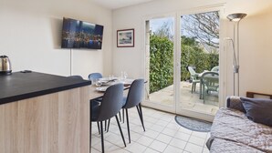 A modern kitchen with a dining area, a TV mounted on the wall, and a sliding glass door leading to an outdoor patio. - Stone house 350m from beach for 4 (Arzon)