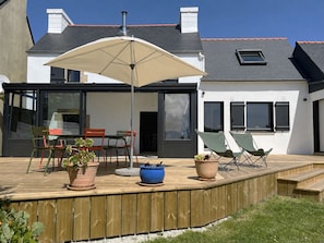 Une terrasse dotée de mobilier d’extérieur, d’un grand parasol et de plantes en pot.