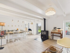 A spacious living area with a high ceiling, a fireplace, a dining table with chairs, and a large window offering a view of the outdoors. - Beach 300m away, house for 7, garden and veranda (Plouguerneau)