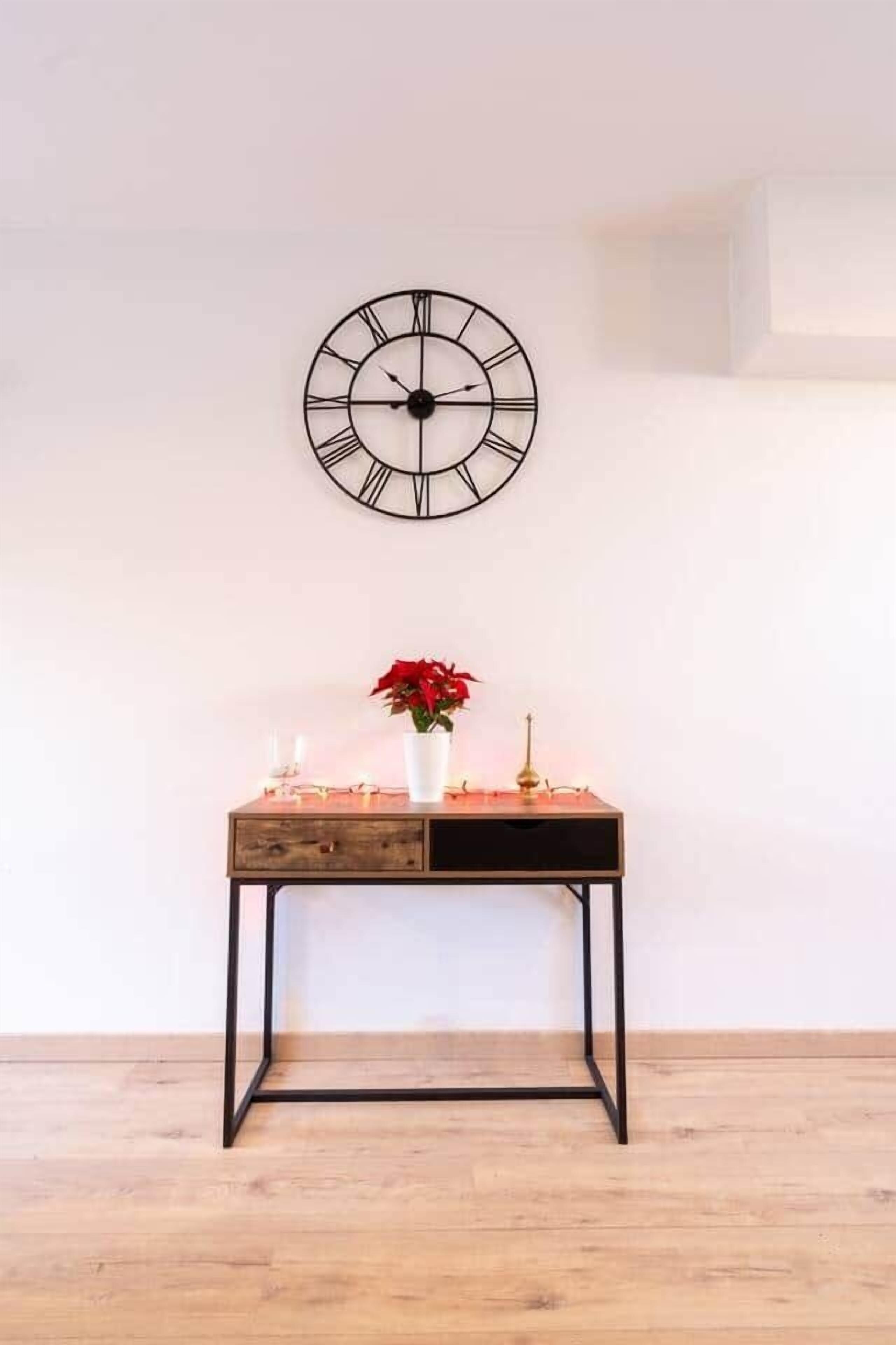 A room with a wooden floor, a wall-mounted clock, a small wooden table with a vase of red flowers, and a candle holder.