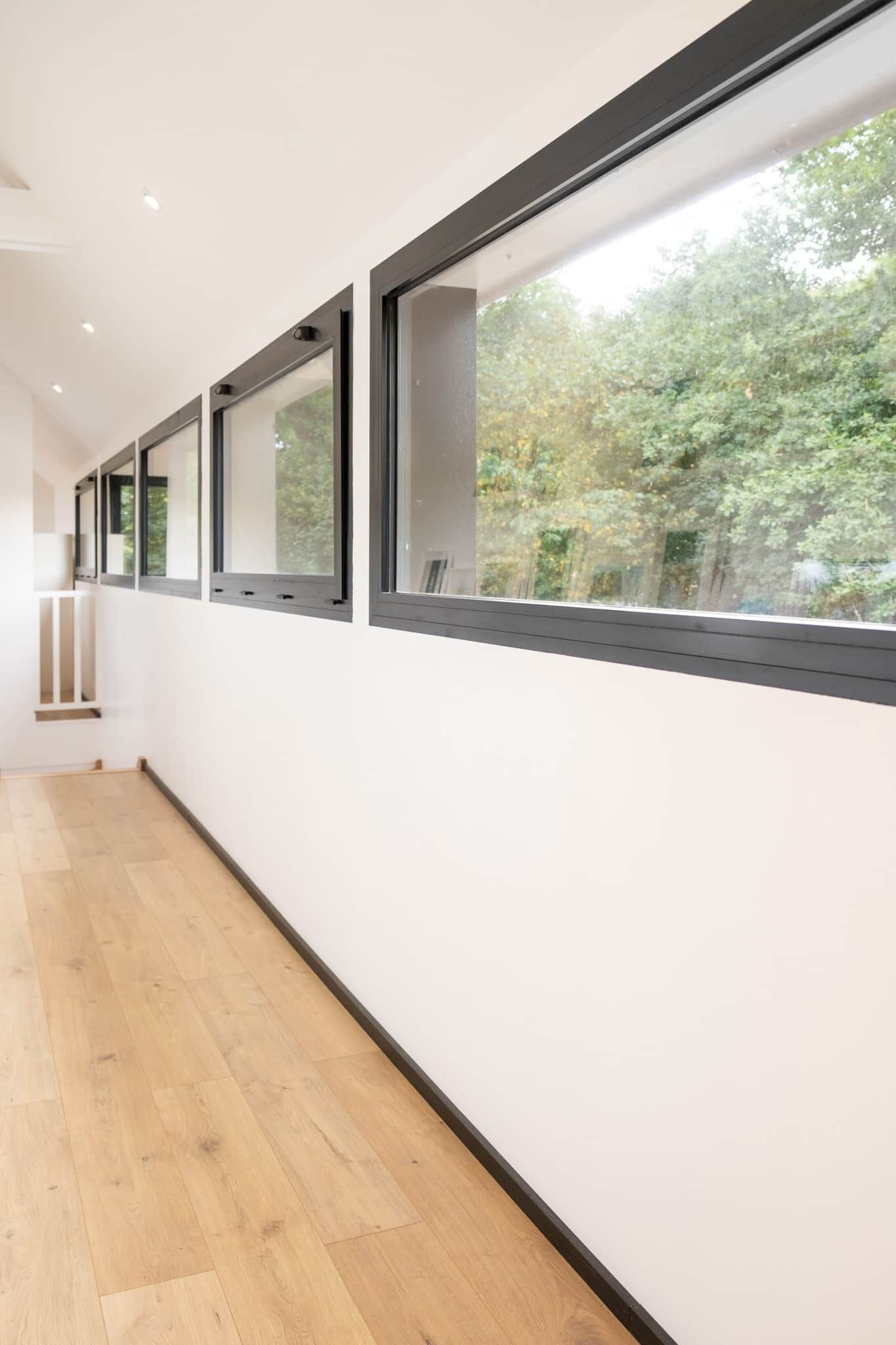 Un couloir doté de grandes fenêtres et d’un plancher en bois.