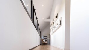 A modern interior with a wooden staircase leading to a second floor, white walls, and a framed picture on the wall. - Architect-designed house in the heart of nature (Guichen)