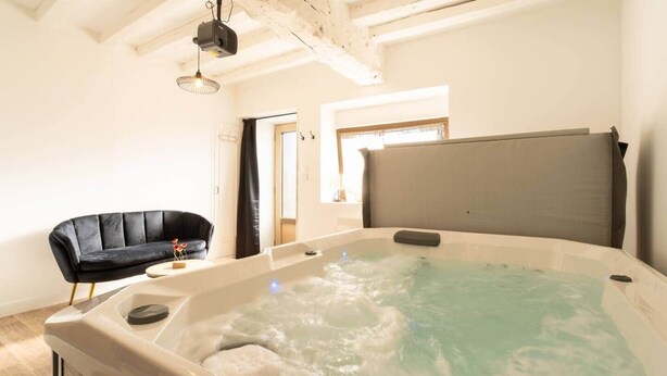 A room with a large hot tub, a black sofa, and a wooden ceiling.