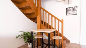 A staircase with wooden steps and a handrail, a small table with two stools, and a potted plant.