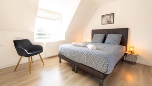A bedroom with a bed, a chair, a bedside table with a lamp, and a window with blinds.