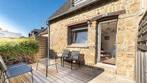 A stone house with a wooden deck, two chairs, and a window.