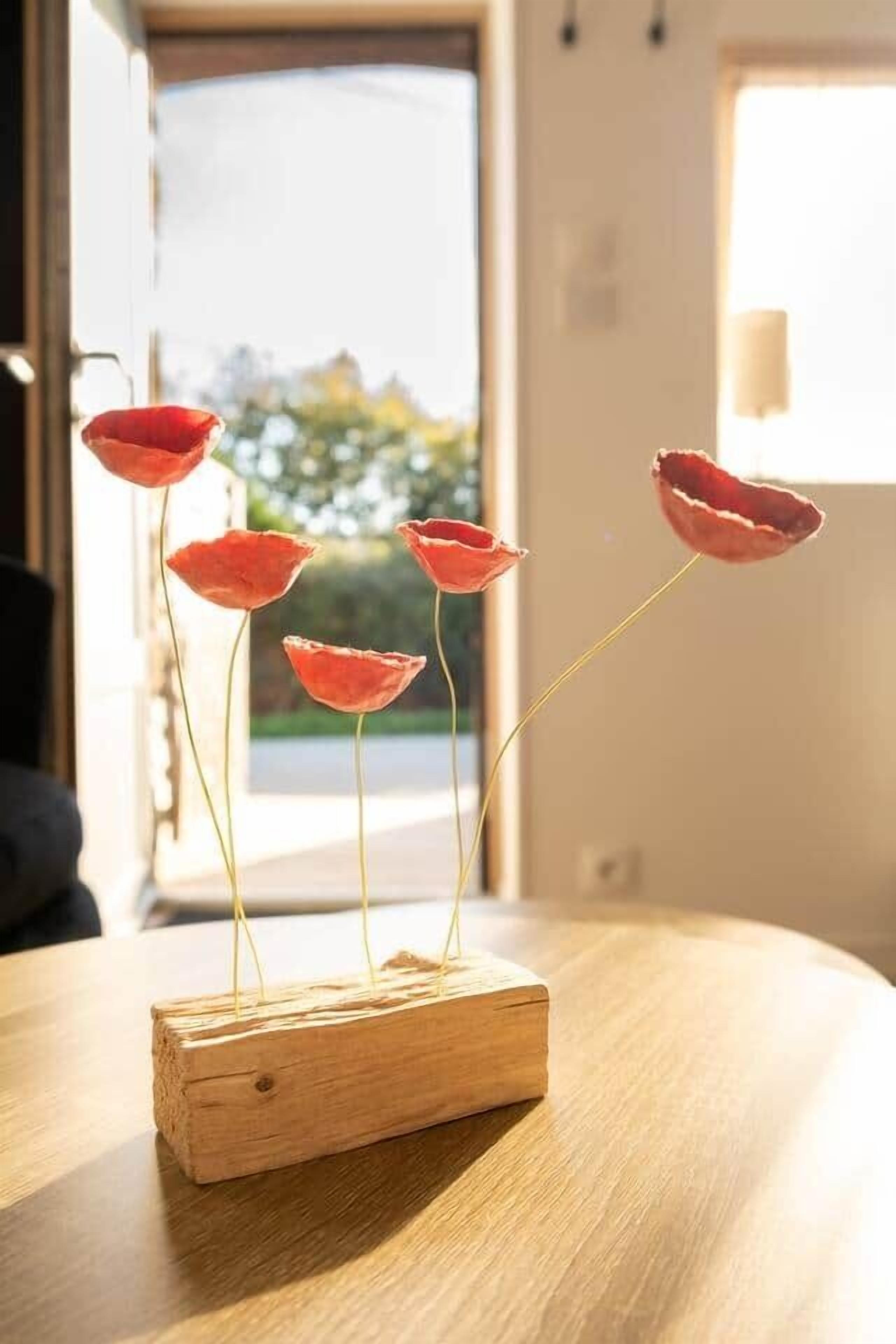 A wooden poppy decoration on a table with a view of a building and a window in the background.