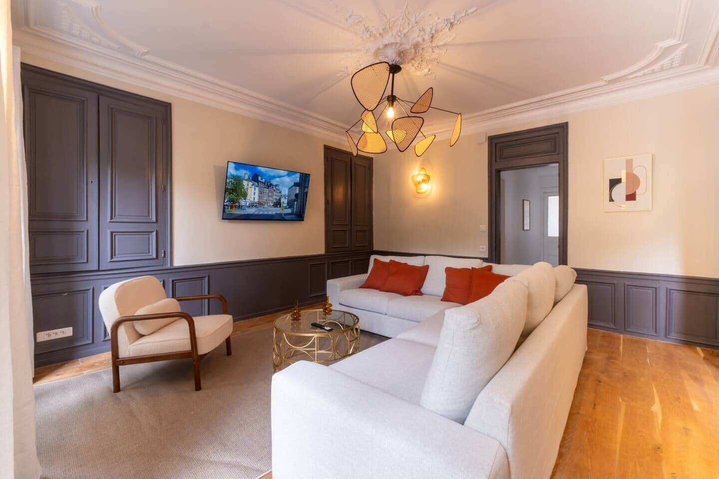 Un salon comprenant un canapé, un fauteuil et une table basse, avec une télévision, un luminaire décoratif et des œuvres d’art accrochées aux murs.