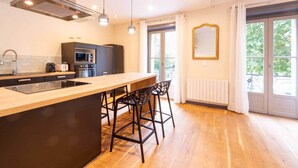 Una cocina moderna con una isla central, taburetes de bar y un gran ventanal que proporciona luz natural.