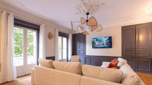Una sala de estar con un sofá color beige, una zona de comedor con armarios de madera oscura y un cuadro con una vista urbana en la pared.
