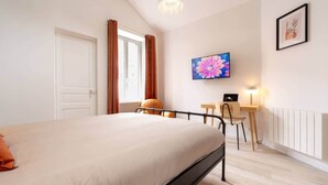 Un dormitorio con cama, escritorio, silla, televisor y radiador.