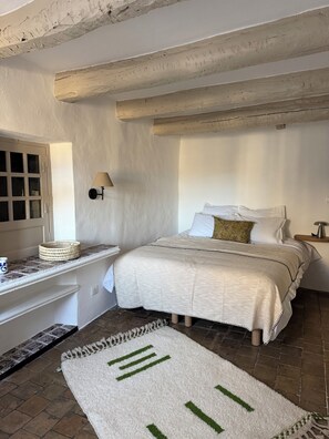 A bedroom with a bed, a nightstand, a lamp, a window, and a door. - Elegant Mediterranean apartment within the historic ramparts of Saint Paul Vence (Saint-Paul-de-Vence)