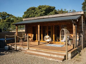 Une cabane en bois dotée d’un porche couvert, de sièges d’extérieur et d’un ventilateur.