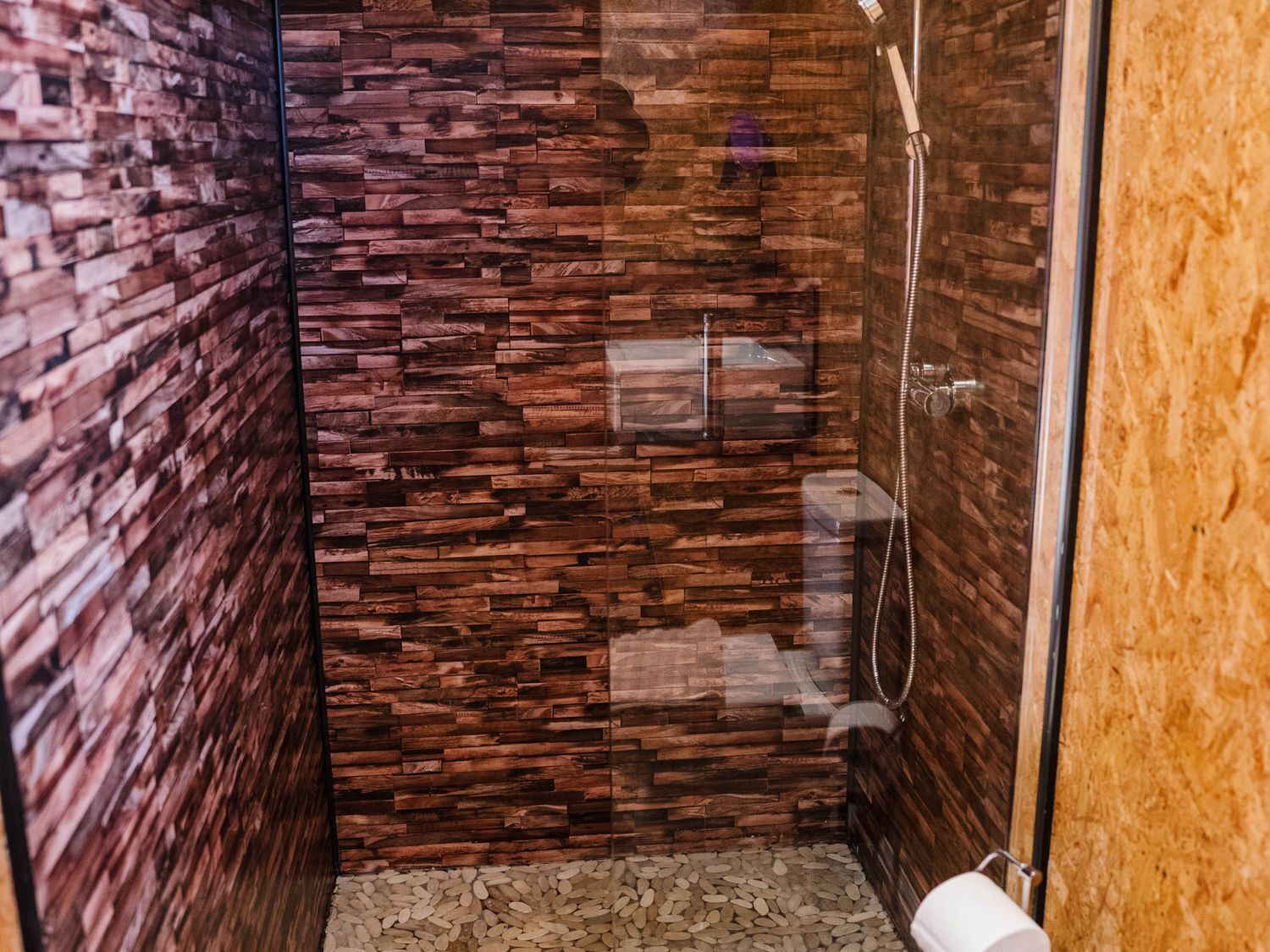 A small, enclosed shower area with a wooden wall design and a glass door.