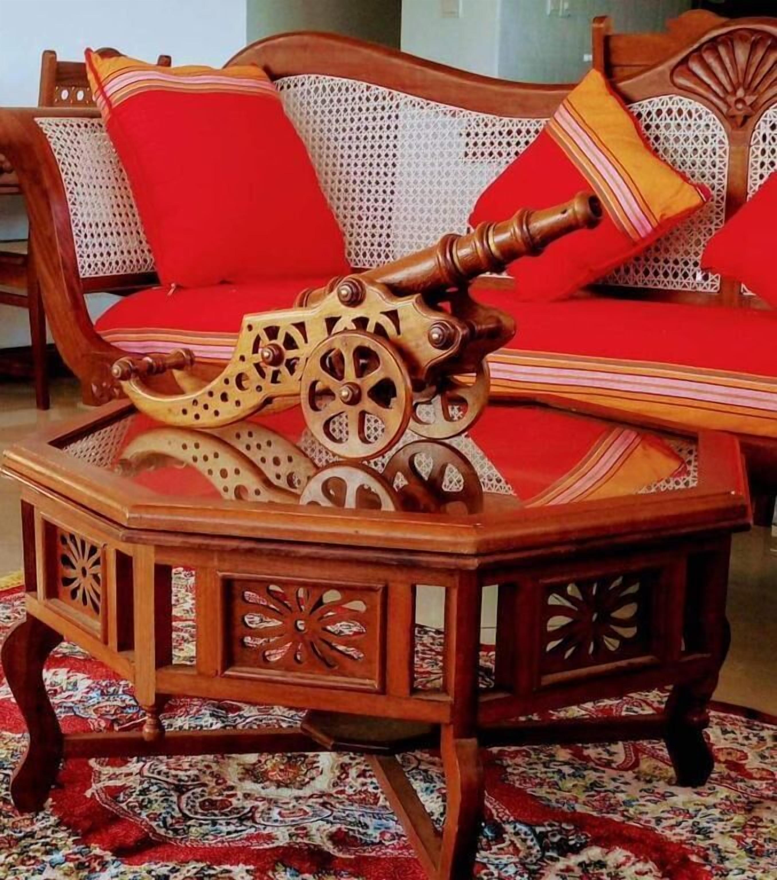 A wooden table with intricate carvings and a vintage-looking mechanical device on top, placed on a patterned rug.