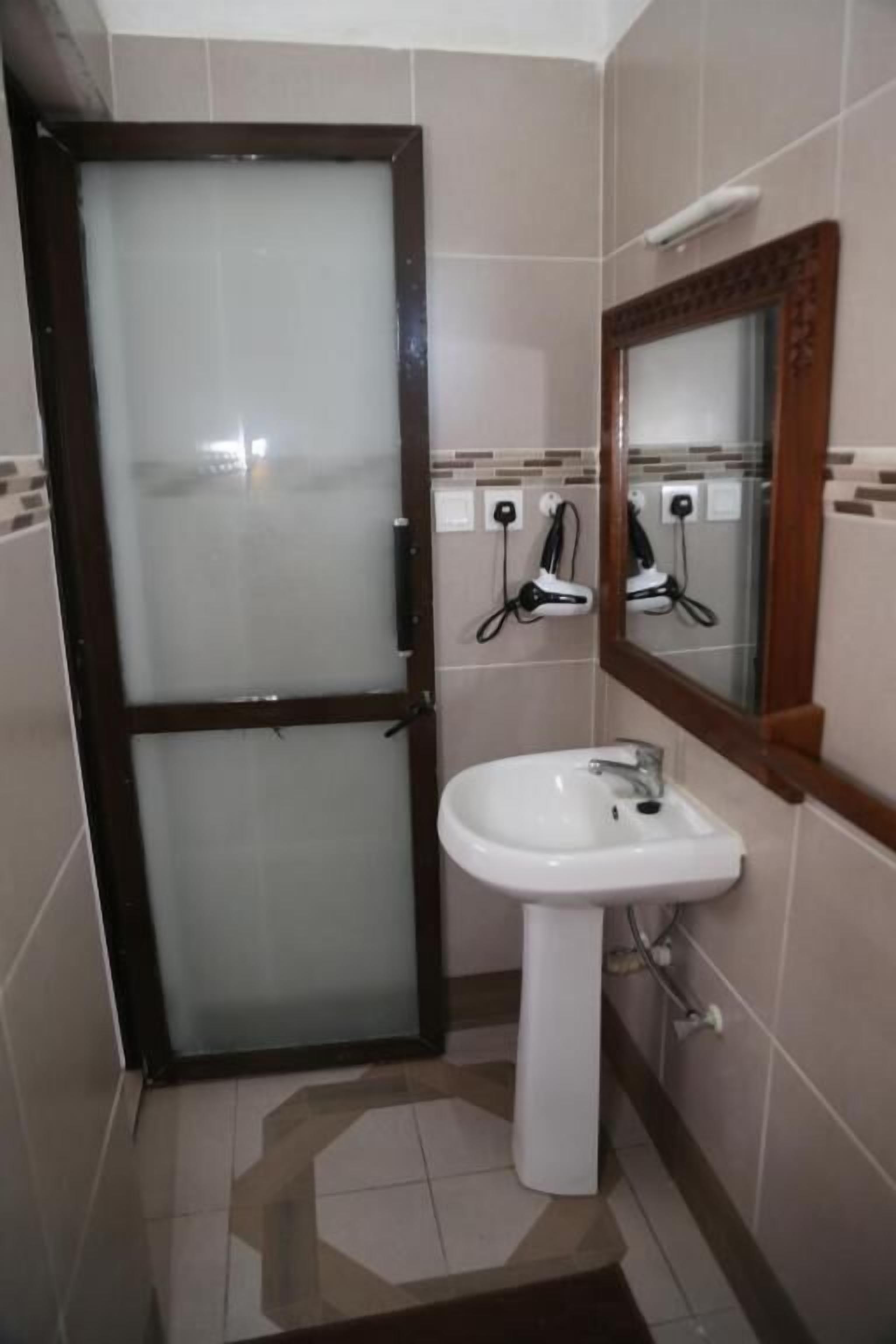 Un bagno con un lavandino bianco, uno specchio con cornice in legno e una porta in vetro satinato.