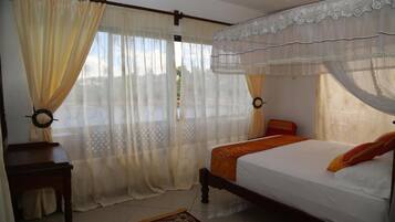 A bedroom with a bed, curtains, a nightstand, and a window with a view.