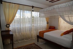 A bedroom with a bed, curtains, a nightstand, and a window with a view.