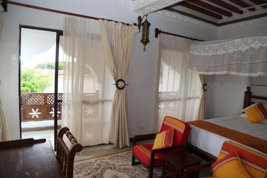 Una camera da letto con un letto, una sedia, un tavolo di legno e un balcone con tende.