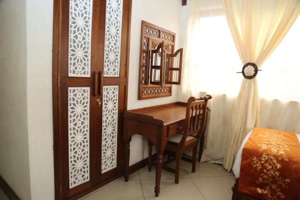 A room with a wooden desk, a chair, a bed with a patterned bedspread, and a decorative wall panel.