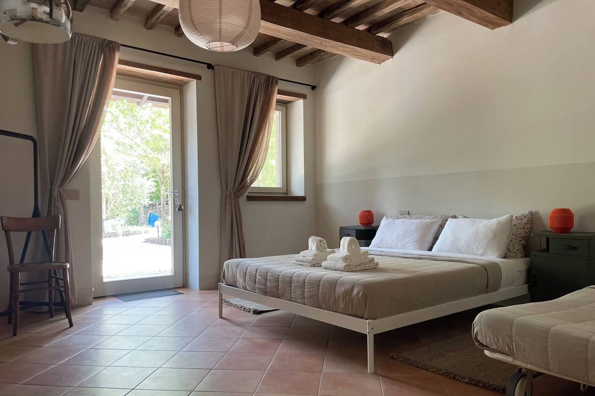 A bedroom with a bed, a chair, a nightstand, and a window.
