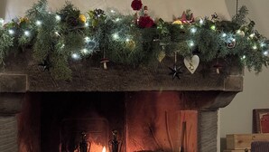 Une cheminée accueillante, ornée d’une guirlande de lumières et de décorations, avec un feu de bois crépitant et une cheminée en pierre rustique.