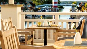 A wooden deck with a table and chairs overlooking a marina with boats and a lighthouse. - Sunday Hafendorf Double Room With Lake-view (Rheinsberg)