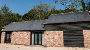 A stone building with a sloped roof and a black door. - The Heronry (Carlisle)
