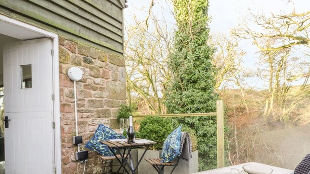 A hot tub area with a stone wall, a wooden door, and a table with chairs. - The Heronry (Carlisle)