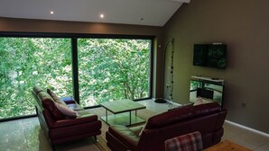 A modern living room with a large window, a flat-screen TV, and a sofa. - The Heronry (Carlisle)
