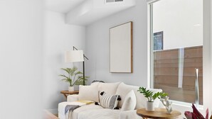 Ein modernes Wohnzimmer mit einem weißen Sofa, einem Holztisch, einer Stehlampe und einem großen Fenster.