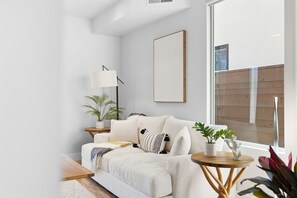 A modern living room with a white sofa, a wooden coffee table, a floor lamp, and a large window. - Elevated Coastal Living | Rooftop Deck Steps from Beach & Restaurants (San Diego)